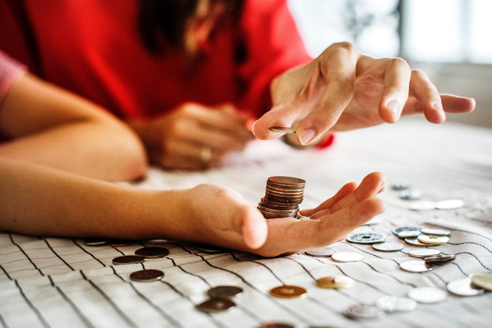 A hand with a stack of coins in the middle, and a woman placing on more coin onto the stack.