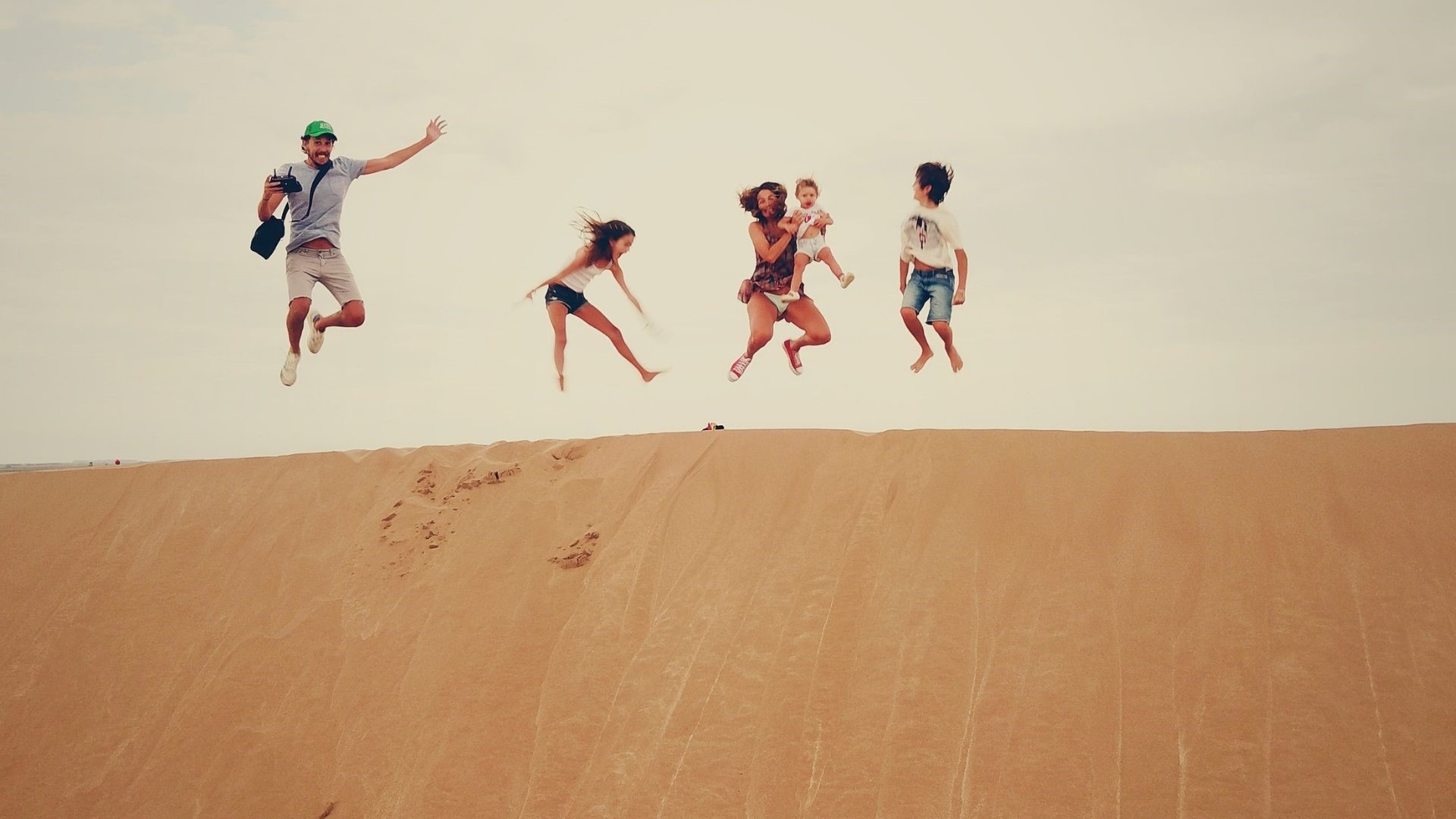 A family on top of a sand dune, jumping in the air. 